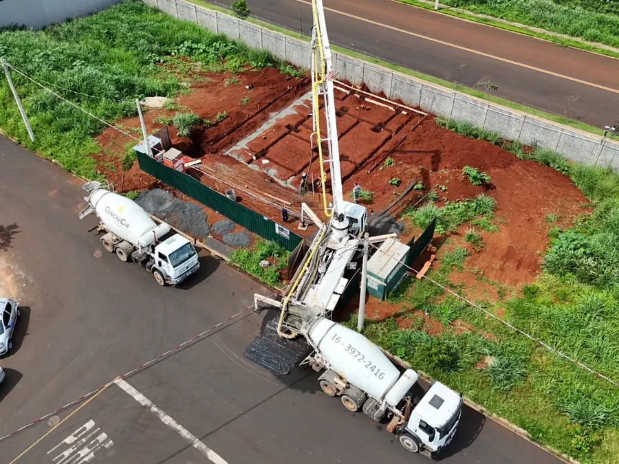 Vista aérea de uma fundação sendo concretada com bomba-lança, com caminhões betoneira da CONCRECIA na rua