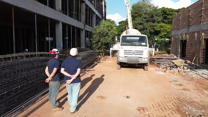 Dois profissionais de capacete observando uma obra, com caminhão betoneira ao fundo
