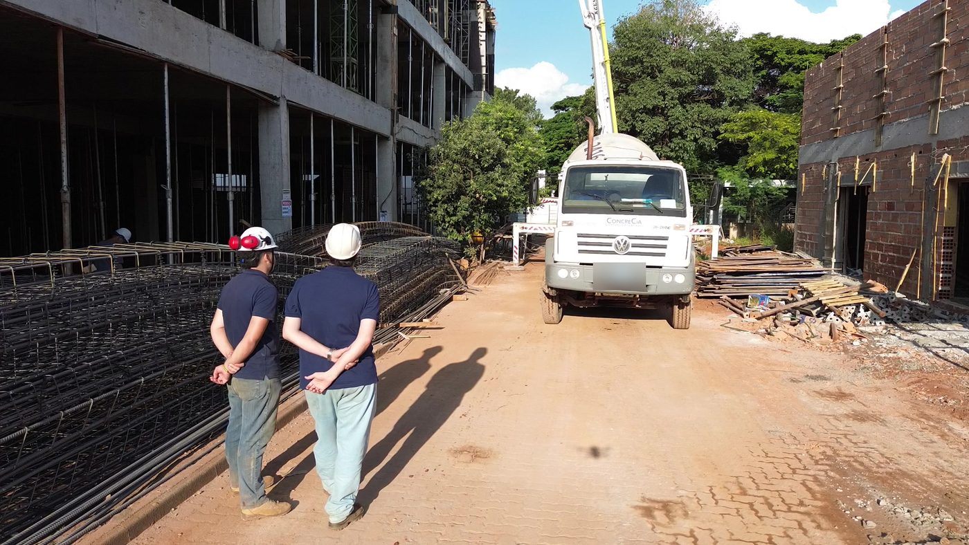 Dois profissionais de capacete em uma obra, com caminhão betoneira da CONCRECIA ao fundo